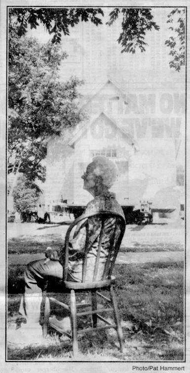 Bertha Smith, 87, sits in the shade of an elm tree at Heritage Square while workers unload the historic Mennoville Church